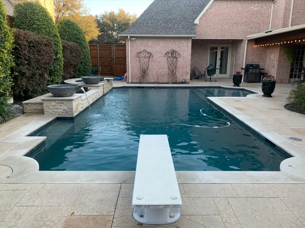 Large rectangular backyard pool with a diving board and brick patio.