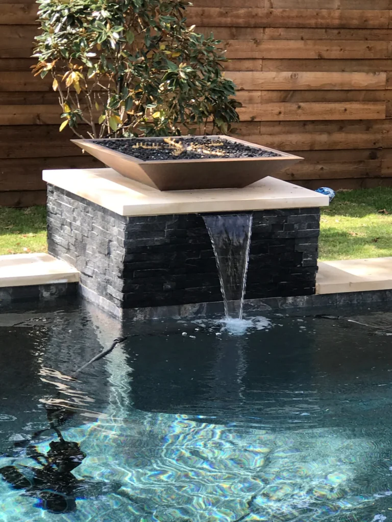 Custom fire and water feature with stone veneer construction waterfall spout and fire bowl design - Leisure Living Pools water feature specialists fire bowl installation luxury outdoor living Dallas Fort Worth Texas