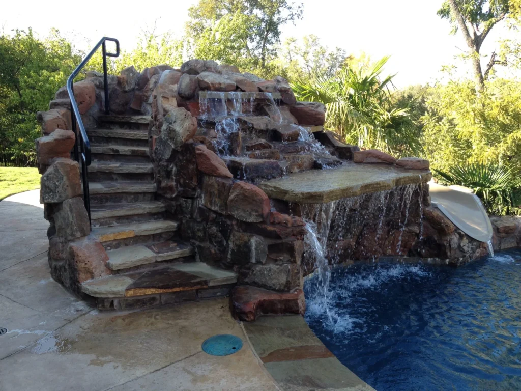 Custom rock waterfall and grotto feature with stone stairs for a freeform pool.